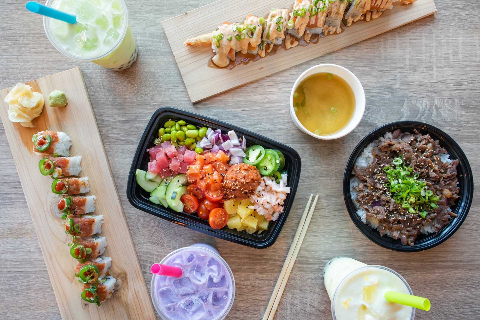 Poke Factory & Ramen Bar spread in Alpharetta: sushi rolls on wood boards, a poke bowl, beef bulgogi rice bowl, miso soup and taro and honeydew bubble tea